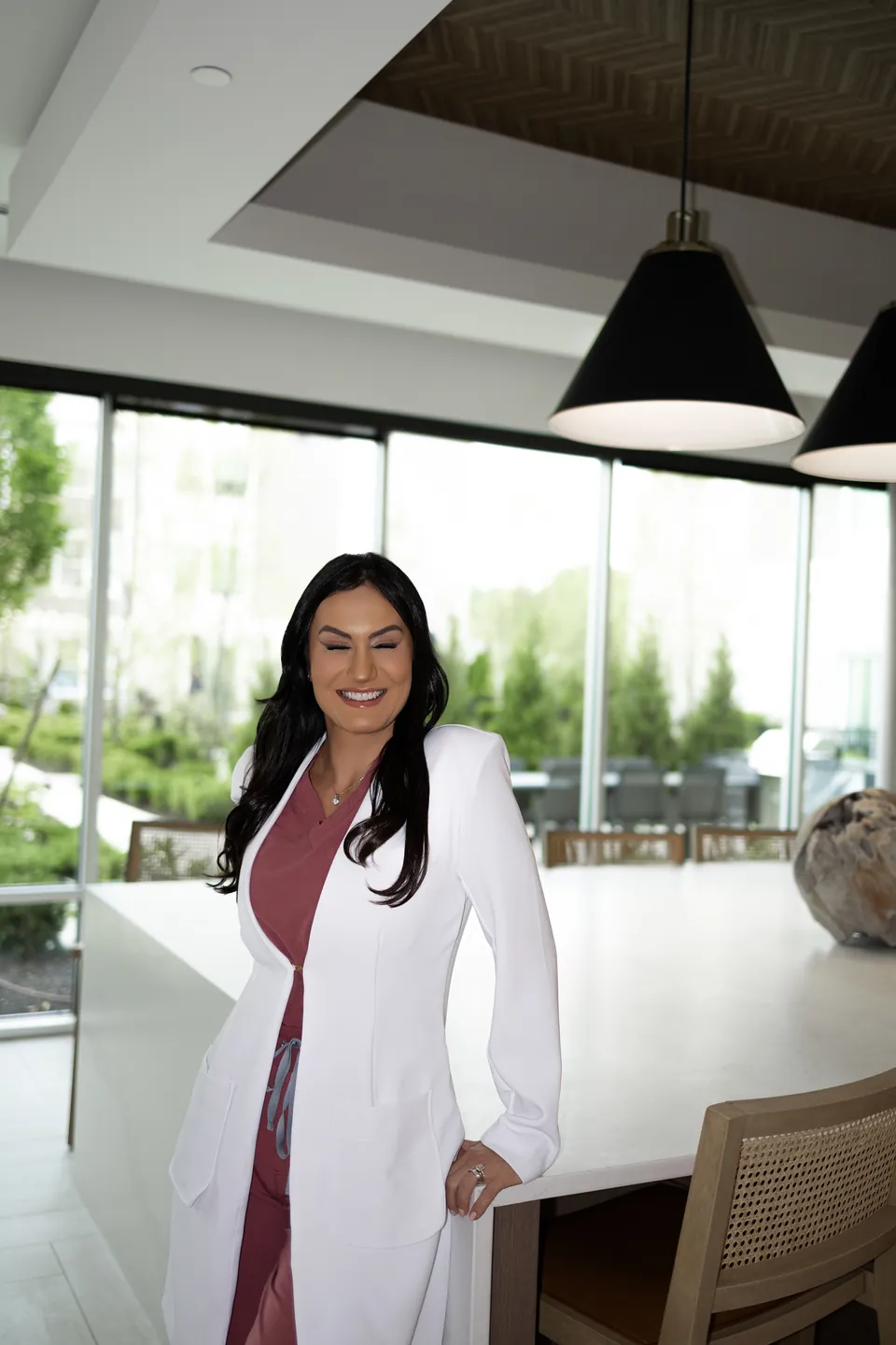 Bianca in a white coat, smiling at a stone counter by the windows