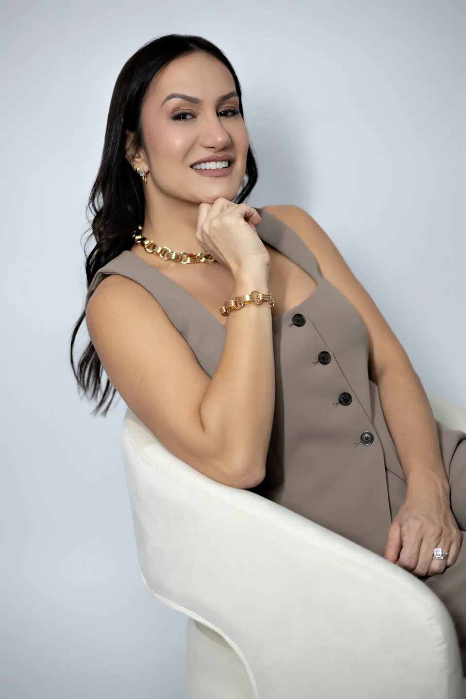 Bianca in a beige vest, smiling with her hand at her chin
