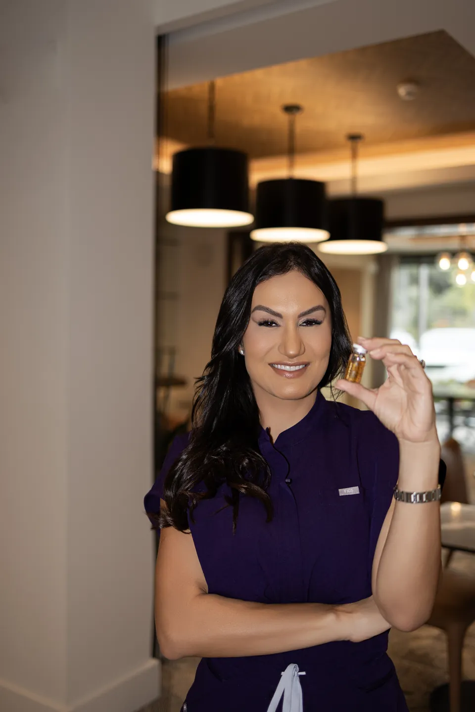 Bianca holding a small vial and smiling in a softly lit lobby